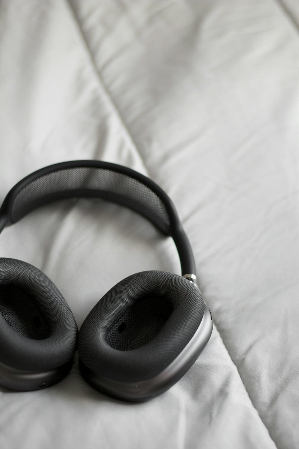 Dark grey over-ear headphones rest on a white quilted surface.